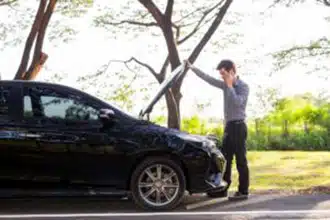 Man In His Phone Looking At A Broken Car